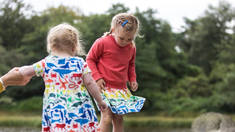 Two young girls balancing and playing by a pond in open countryside